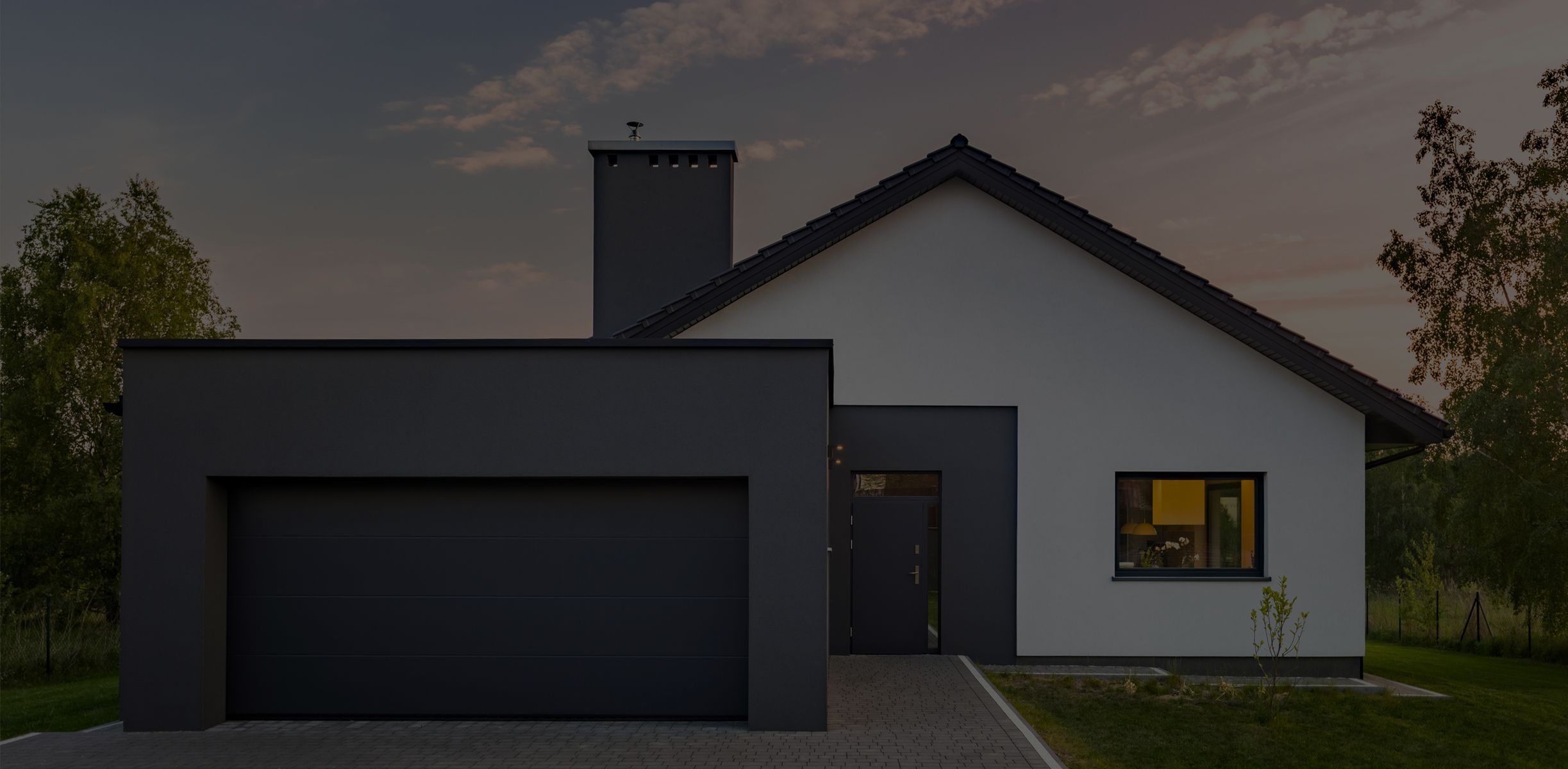 Modernes Einfamilienhaus mit weißer Fassade, dunkler Garage und Satteldach in grüner Umgebung